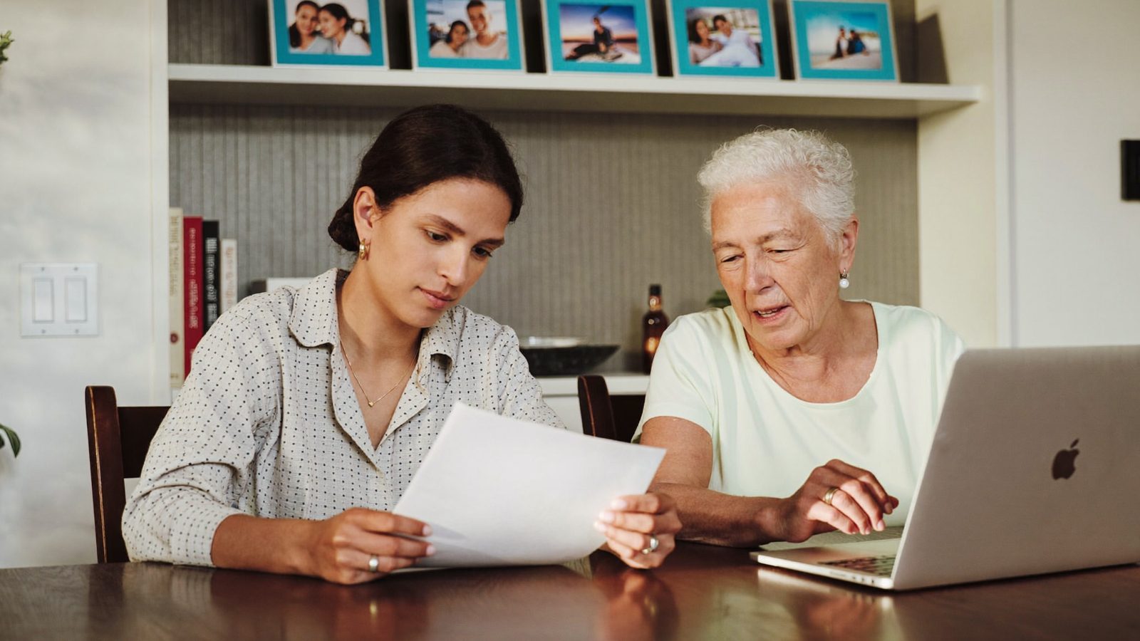 Adult daughter and her senior mother reviewing paperwork together at a dining table