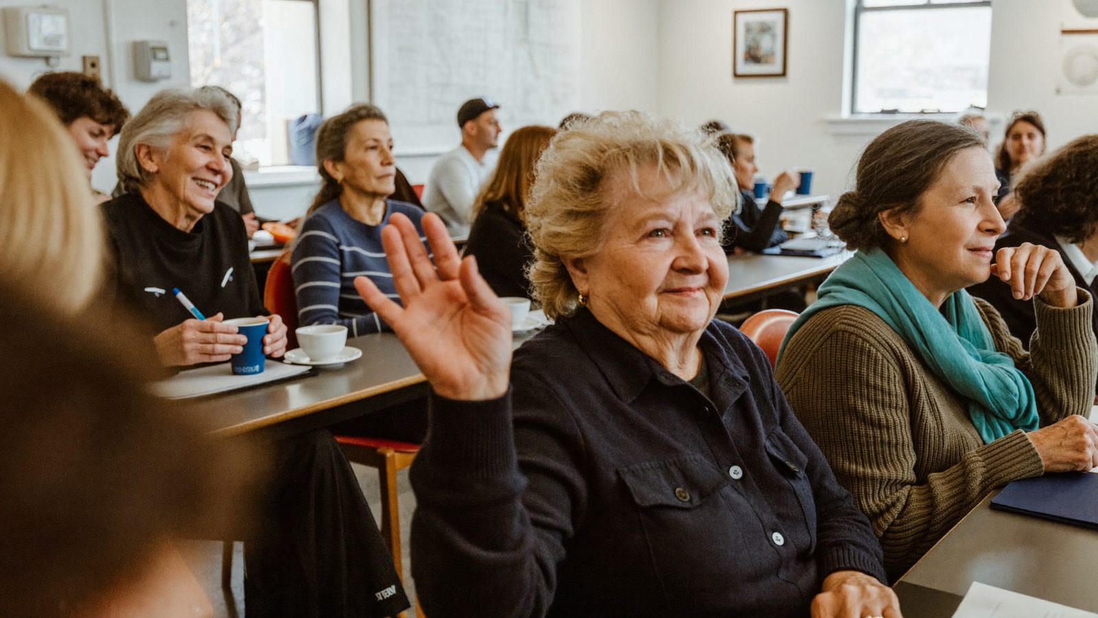 Seniors with notepads at a friendly community education session, one woman raising her hand