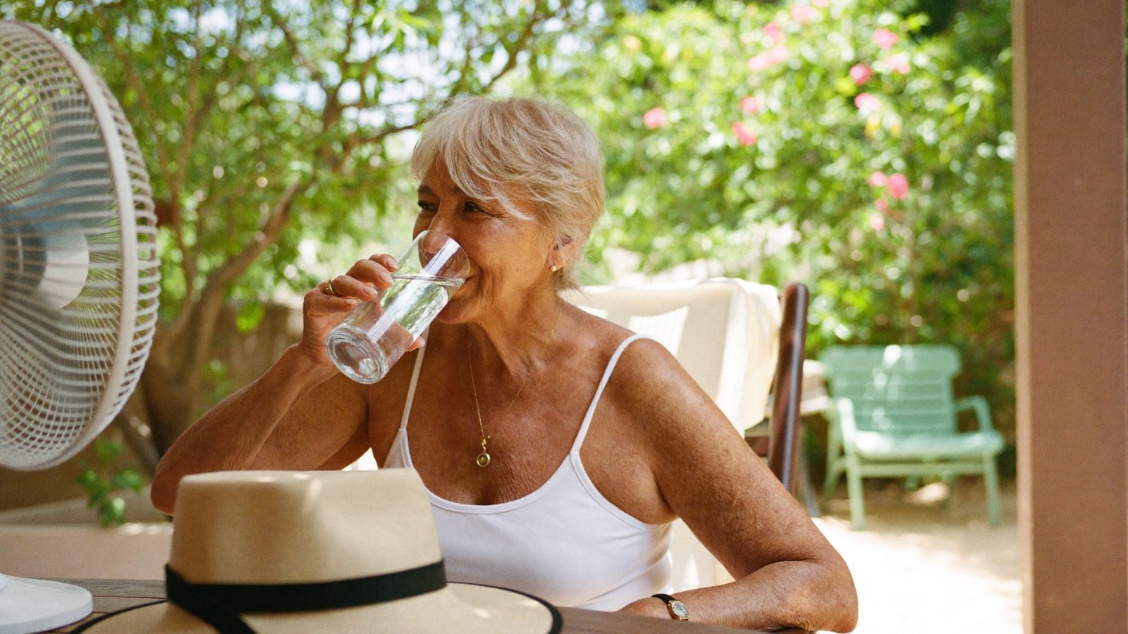 Senior woman staying cool with a glass of ice water on a shaded summer patio