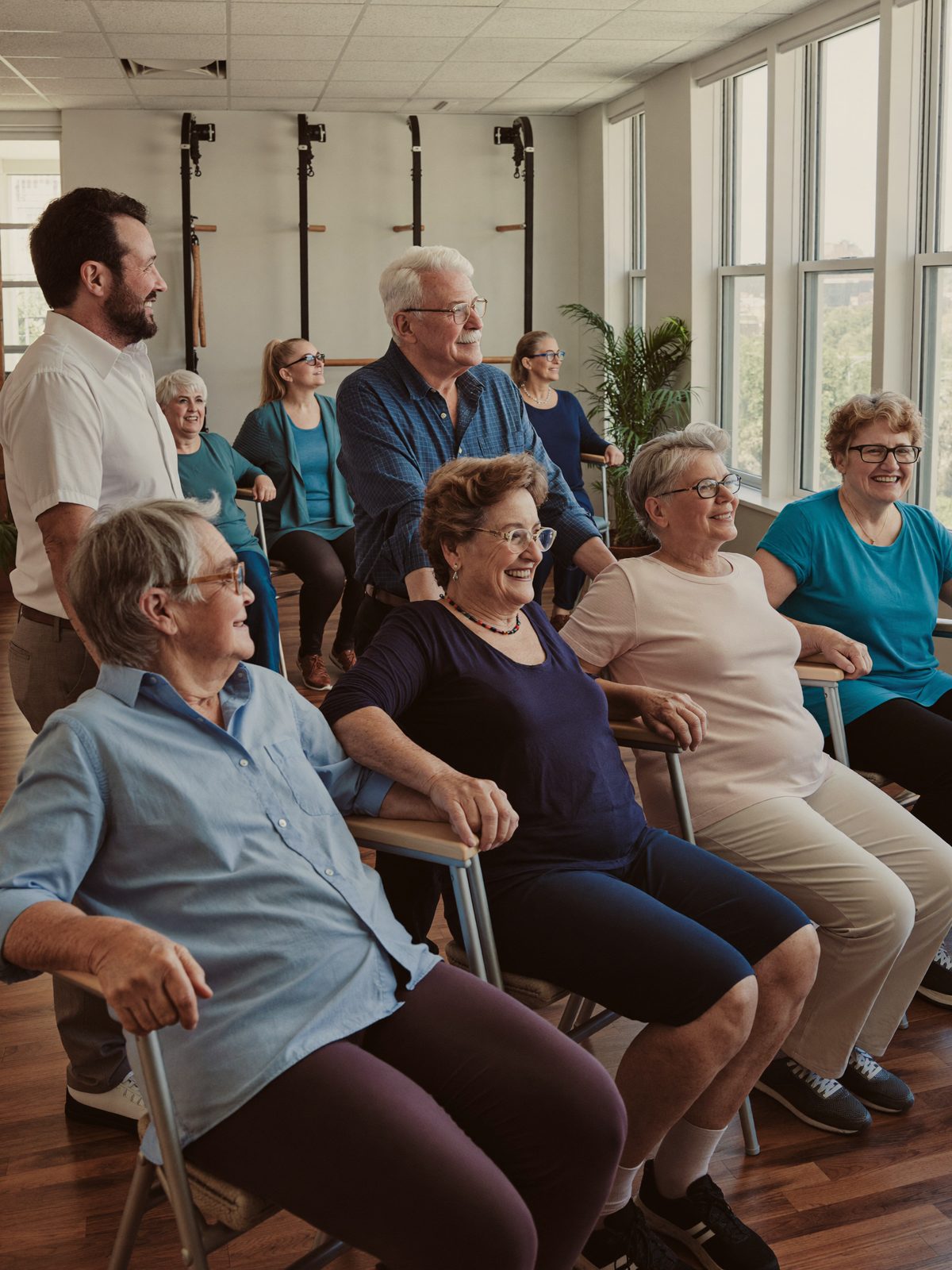 Seniors practicing gentle chair-assisted balance exercises together in a bright community activity room